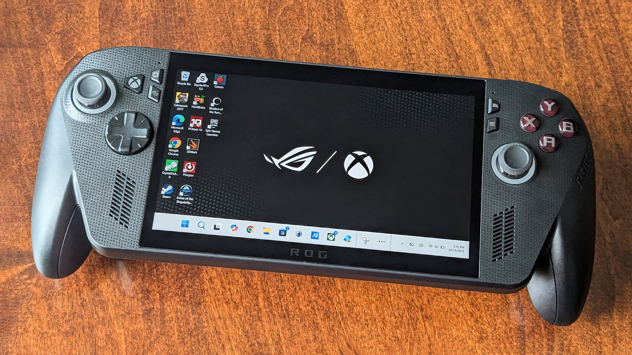 Xbox Ally X lying on its back on a table with the Windows desktop showing on its screen. 